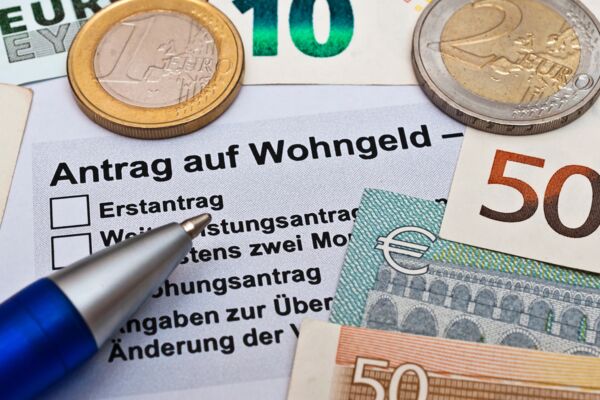 Wohngeldantrag-Formular, umgeben von Euro-Münzen und -Scheinen, verdeutlicht finanzielle Unterstützungsmöglichkeiten für Mieter.