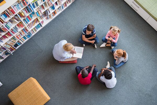 Ein Bild von Kindern verschiedener Herkunft, die zusammen in einer Bibliothek sitzen und lesen, was die Bedeutung von Bildung und Inklusion betont.