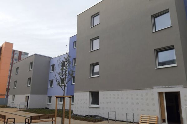 Ein renovierter Wohnblock mit moderner Fassade in verschiedenen Farben, umgeben von einer gepflegten Umgebung.