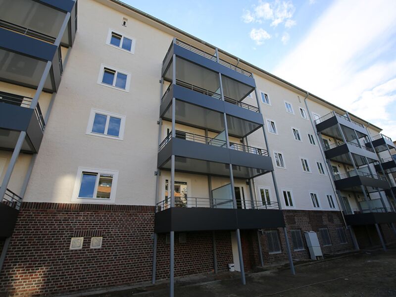 Bild der Außenseite eines modernen, mehrstöckigen Wohngebäudes mit Balkonen, charakterisiert durch die kontrastreiche weiße Fassade und die Verwendung von dunklen Metallelementen.