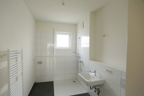 Ein sauberes und einfaches Badezimmerdesign mit weißer Fliesenverkleidung, begehbarer Dusche und natürlichem Licht, das Funktionalität und moderne Ästhetik betont.