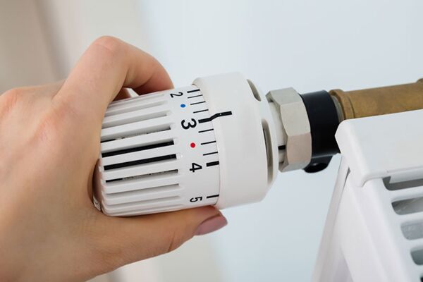 Ein Bild einer Hand, die ein Heizkörperventil einstellt, illustriert energiesparende Maßnahmen im Haushalt.
