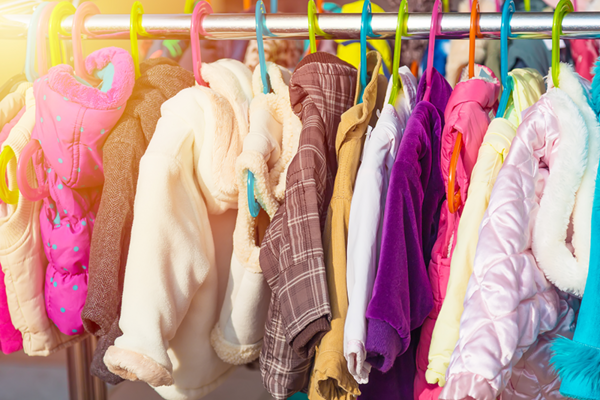 Ein helles und farbenfrohes Bild von Kinderjacken, die auf Kleiderbügeln hängen, was auf eine Außen- oder Kleidungsspendenaktion hinweisen könnte.