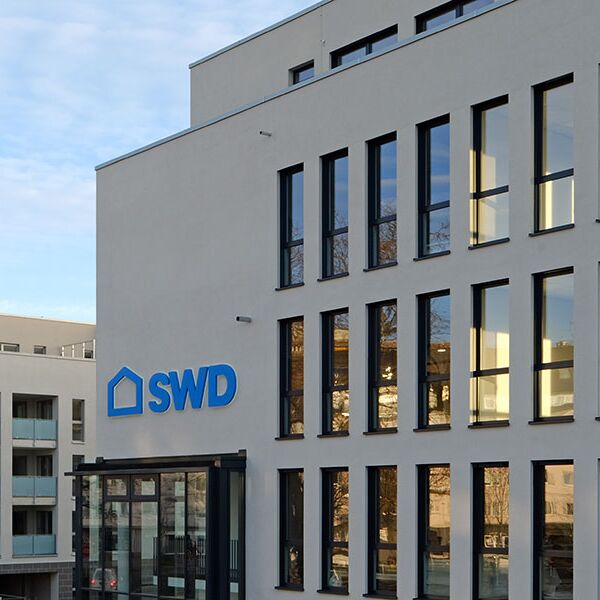 Ein modernes Bürogebäude mit der Aufschrift "SWD" am Eingang. Das Gebäude hat eine minimalistische Architektur mit weißen Wänden und großen Fenstern, die einen zeitgenössischen Look vermitteln.