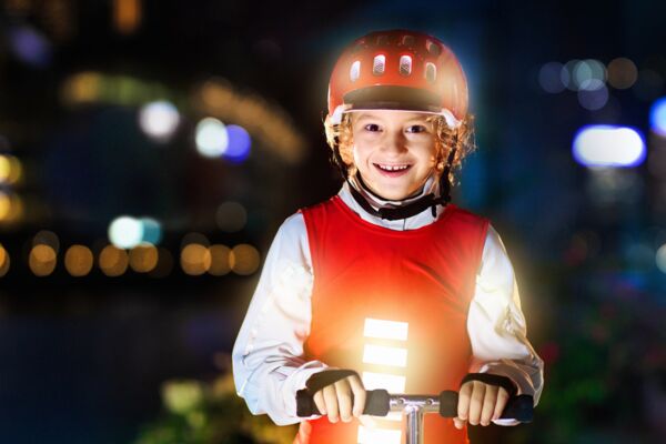 Ein fröhliches Kind mit Schutzkleidung und reflektierendem Helm, bereit für eine sichere Fahrt in einer urbanen Nachtlandschaft.