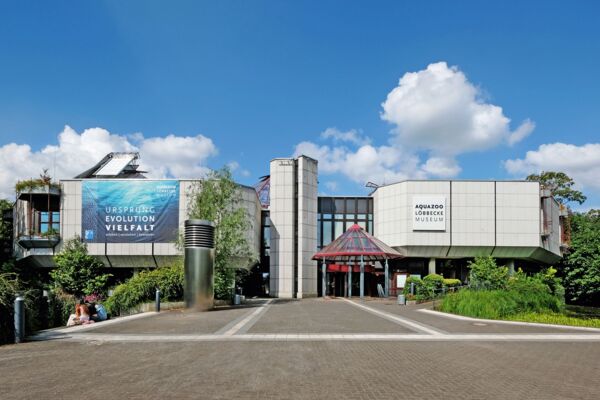 Das Eingangsgebäude des Aquazoos mit einem Werbebanner, das die biologische Vielfalt und Evolution thematisiert, lädt Besucher ein, die Wunder der Unterwasserwelt zu entdecken.