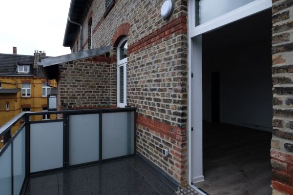 Balkon eines Altbauwohnhauses mit Blick auf benachbarte Dächer, ausgestattet mit modernen Geländern und neuem Zugang.