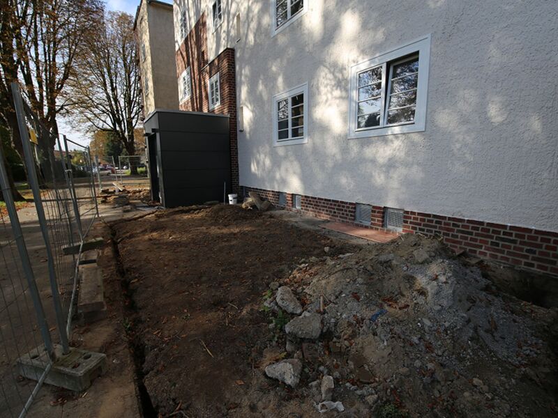 Bild der Baustelle neben einem frisch renovierten Gebäude, zeigt Erdaushubarbeiten und Baugeräte.