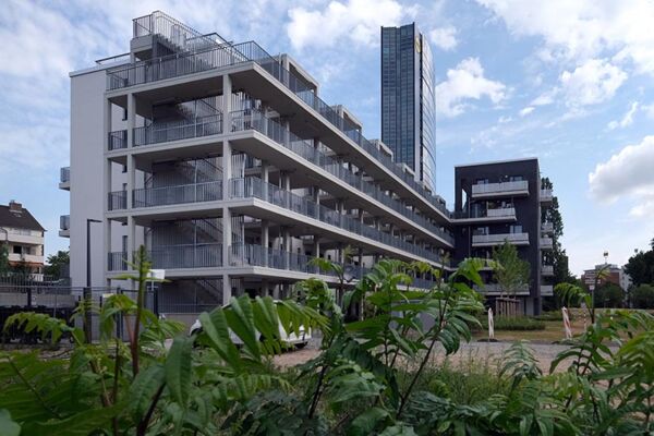 Außenansicht eines modernen Wohnkomplexes mit offenem Treppendesign, eingebettet in ein grünes Umfeld. Die Architektur hebt sich durch ihre klare Struktur hervor.