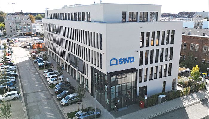 Verwaltungsgebäude der SWD mit großflächigen Fenstern und einem klaren, weißen Design. Der Eingangsbereich ist gut sichtbar, umgeben von einem Parkplatz.