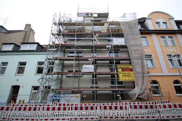 Das Foto dokumentiert die Sanierung eines Stadthauses, umgeben von einem Gerüst und Bauzäunen, in einem lebendigen städtischen Viertel. Die Fassade des Gebäudes wird modernisiert, was eine wesentliche Aufwertung für die Straße darstellt.