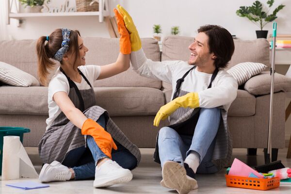 Ein junges Paar hat Spaß beim Putzen ihres Wohnzimmers, ein Beispiel für Teamarbeit und häusliche Pflege.