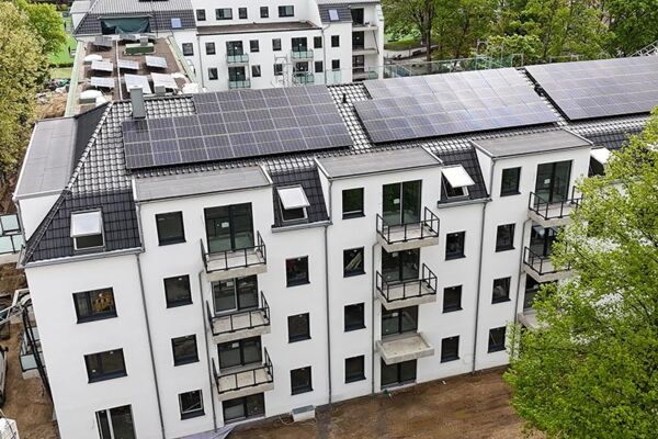 Luftaufnahme eines Neubaus mit Solarpanelen auf dem Dach. Die Gebäudeplanung vereint moderne Architektur mit umweltfreundlicher Energie.