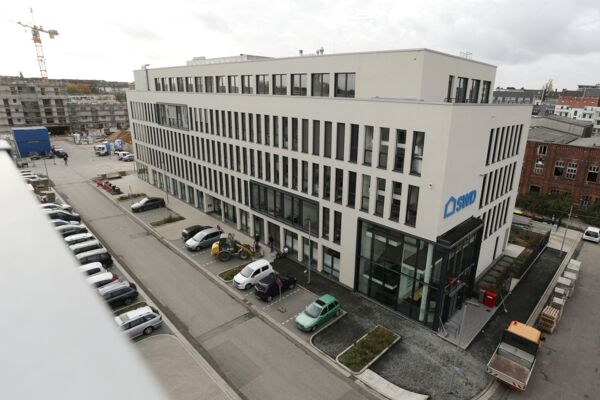 Modernes Firmengebäude von einer erhöhten Perspektive aus fotografiert, zeigt Parkplatz und umliegende Bebauung.