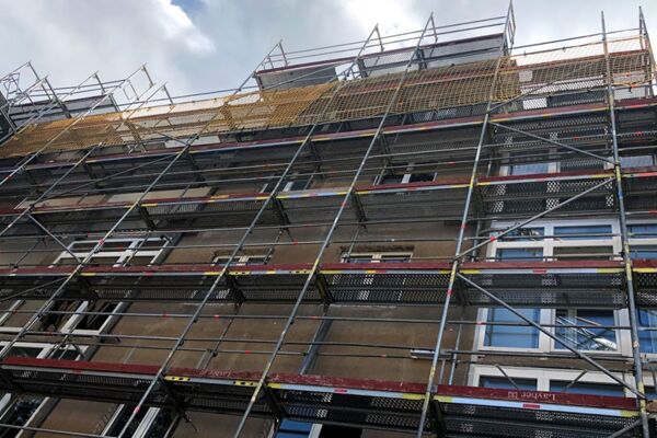 Baugerüst an einem großen Gebäude mit mehreren Stockwerken, das auf umfangreiche Renovierungsarbeiten hindeutet.