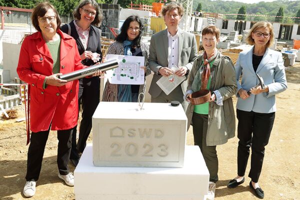 Eine Gruppe von Personen steht zusammen bei einer Grundsteinlegung, mit einer Plakette, die das Jahr 2023 anzeigt, und feiert den Baubeginn.