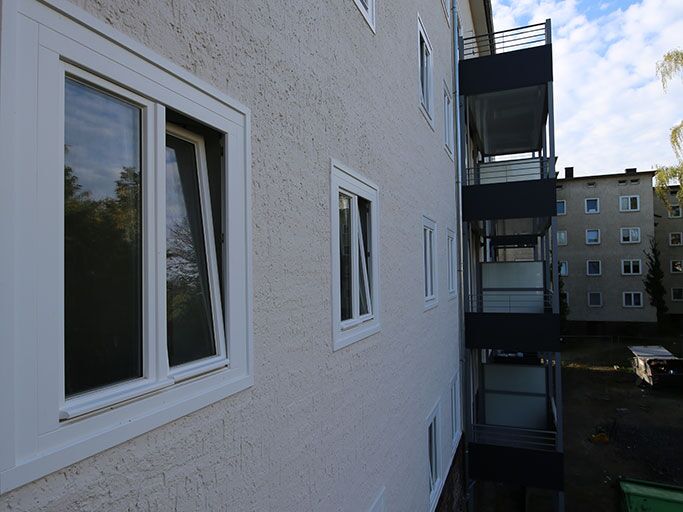 Außenansicht eines mehrstöckigen Wohngebäudes mit Balkonen, weißer Fassade und einer auffälligen roten Ziegeltrennung am Sockel.