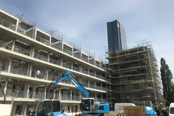 Ein Bild von einem im Bau befindlichen Mehrfamilienhaus, das die dynamische Entwicklung urbanen Wohnraums zeigt, mit einem Kran und Bauarbeitern in Aktion.