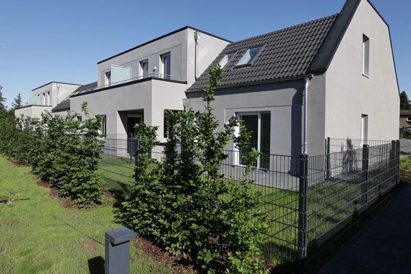 Ein Bild von modernen Reihenhäusern mit gut gepflegten Vorgärten, die ein Beispiel für zeitgenössische Wohnarchitektur in suburbanen oder städtischen Umgebungen bieten.