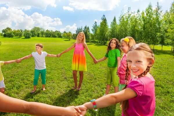 Ein Bild von Kindern, die im Kreis auf einer Wiese stehen und sich an den Händen halten, symbolisch für Freundschaft und gemeinsame Freude in einer natürlichen Umgebung.