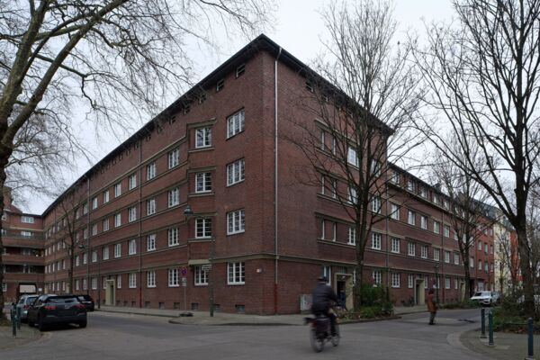 Ein großes, traditionelles Backsteingebäude in einem Wohngebiet, umgeben von Bäumen und wenig Verkehr.