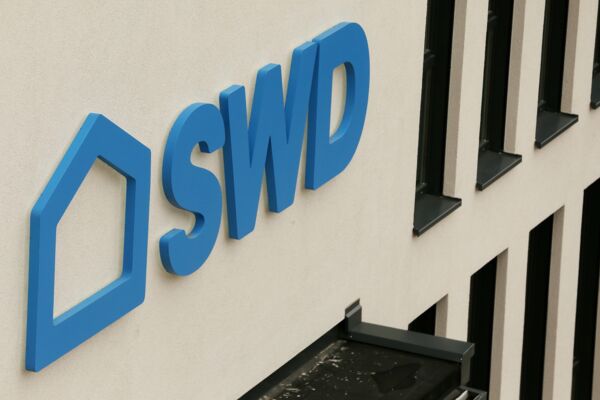 Nahaufnahme des Firmenschilds "SWD" an einem modernen Bürogebäude mit streifenförmigen Fenstern.
