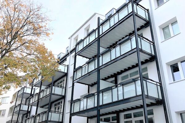 Moderne Wohnanlage mit mehreren Ebenen von Balkonen, hervorgehoben durch die Herbstbäume im Vordergrund.