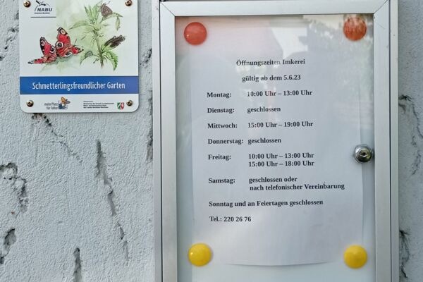 Ein Aushang mit den Öffnungszeiten einer Imkerei, begleitet von einem Hinweis auf einen schmetterlingsfreundlichen Garten.