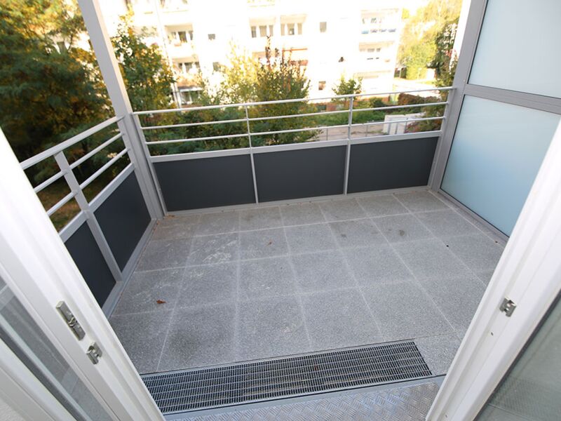 Bild eines leeren Balkons in einem modernen Gebäude, umgeben von Bäumen und mit einem Blick auf die angrenzende Wohngegend.