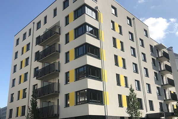 Ein neues Apartmentgebäude mit einem auffälligen gelben und grauen Farbschema. Das Gebäude bietet Balkone und eine klare, blockhafte Struktur, die urbanes Wohnen in einer modernen Umgebung widerspiegelt.