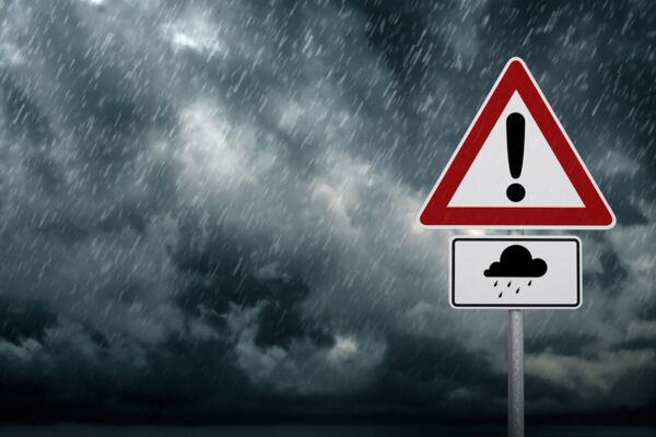 Ein Warnschild für schlechtes Wetter mit Regen und Sturm im Hintergrund, unter einem dramatischen, dunklen Himmel.