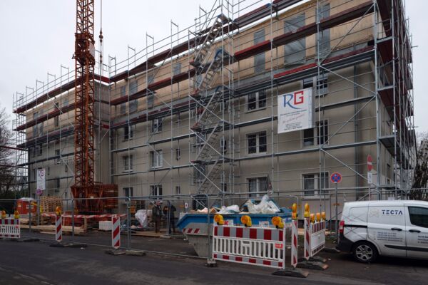 Mehrfamilienhaus im Bau mit umfassender Gerüststruktur und einem Turmdrehkran auf der Baustelle. Modernisierungs- und Bauarbeiten in einem städtischen Wohngebiet.