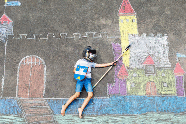 Ein kreatives Bild eines Kindes, das als Ritter verkleidet ist und auf einer mit Kreide gezeichneten Burg spielt, zeigt Kinderspiel und Fantasie.