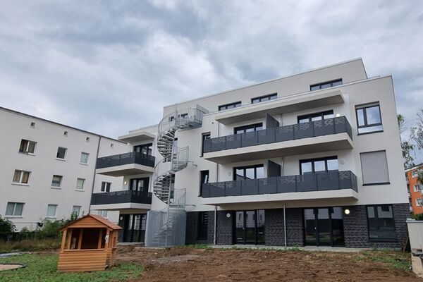 Foto einer neu gebauten Wohnanlage mit moderner Architektur und einer spiralförmigen Außentreppe, die Ästhetik und Funktionalität in städtischem Wohnungsbau zeigt.