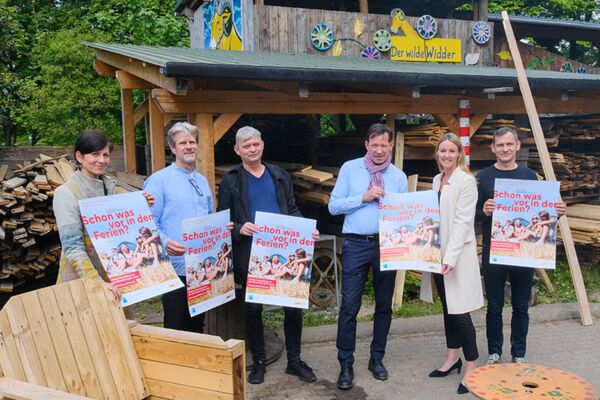 Ein Bild von Vertretern einer Gemeinde, die Werbeplakate für Sommeraktivitäten für Kinder und Jugendliche präsentieren, was die Förderung lokaler Freizeitprogramme hervorhebt.