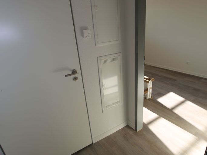 Foto eines hell beleuchteten leeren Zimmers mit geschlossener weißer Tür und Holz-Laminatboden.