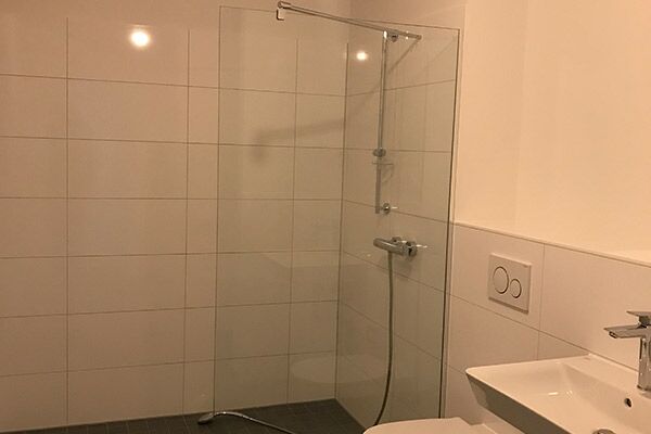 Geräumiges, weiß gefliestes Badezimmer mit einer bodenebenen Dusche und moderner Sanitärausstattung.