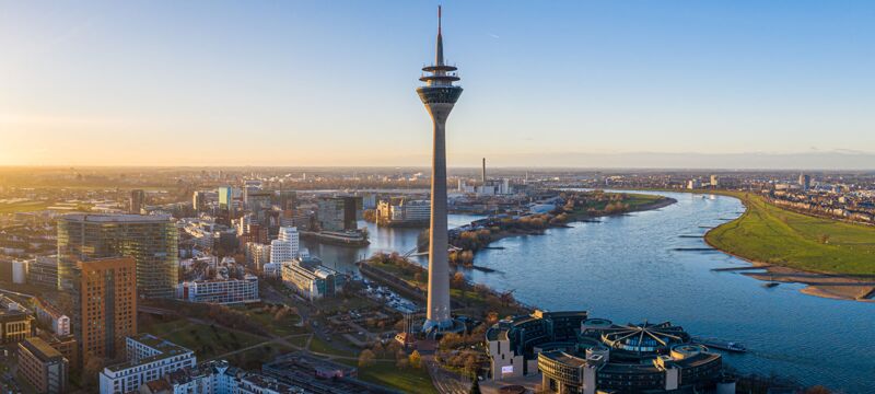 Stadtansicht von Düsseldorf mit dem Rheinturm und dem Rhein im Hintergrund, aufgenommen bei Sonnenuntergang.