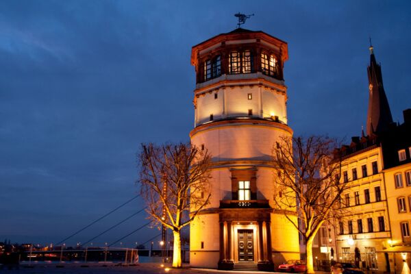 Ein stimmungsvolles Foto eines beleuchteten Turms bei Nacht, eingefangen in einer städtischen Umgebung mit blauem Abendhimmel im Hintergrund.