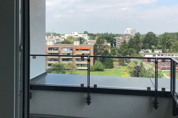 Blick von einem Balkon aus auf eine urbane Landschaft mit Wohngebäuden und begrünten Flächen.