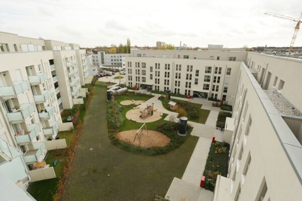 Luftaufnahme eines Wohnkomplexhofes, der schön mit Gehwegen, Spielbereichen und gemeinschaftlichen Treffpunkten inmitten moderner Wohnblöcke gestaltet ist.