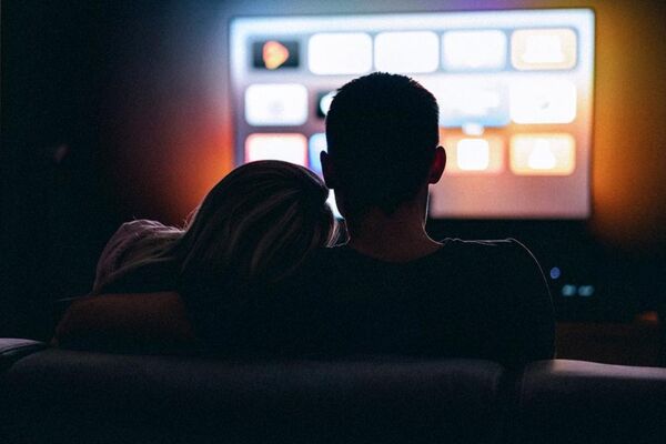 Ein Paar sitzt gemeinsam auf dem Sofa und sieht fern, mit einem gemütlichen und stimmungsvollen Licht im Hintergrund.