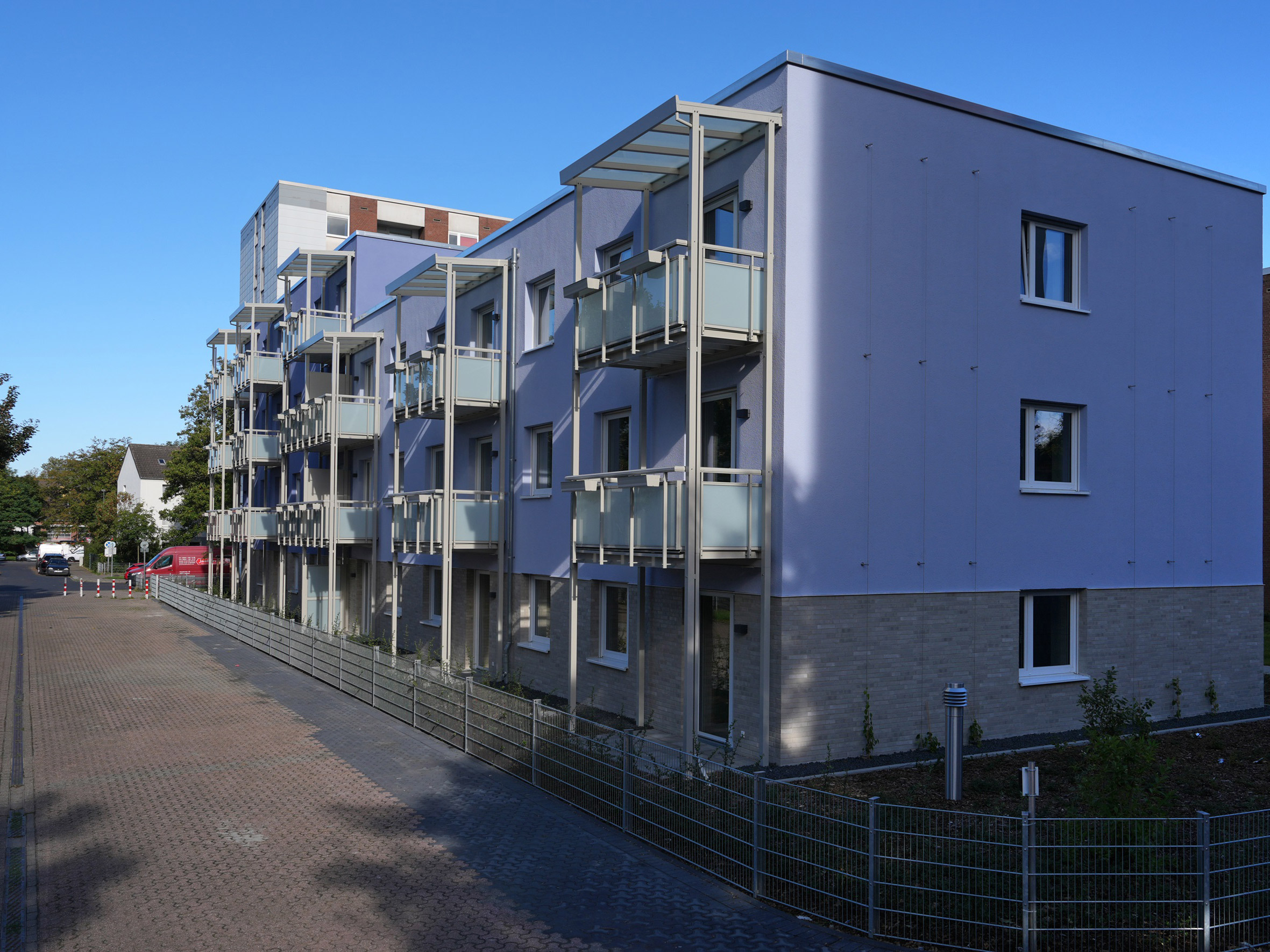 Modernes Mehrfamilienhaus mit einer Fassade in hellen und dunklen Tönen, versehen mit Balkonen und bodentiefen Fenstern, die in eine ruhige Straße führen.