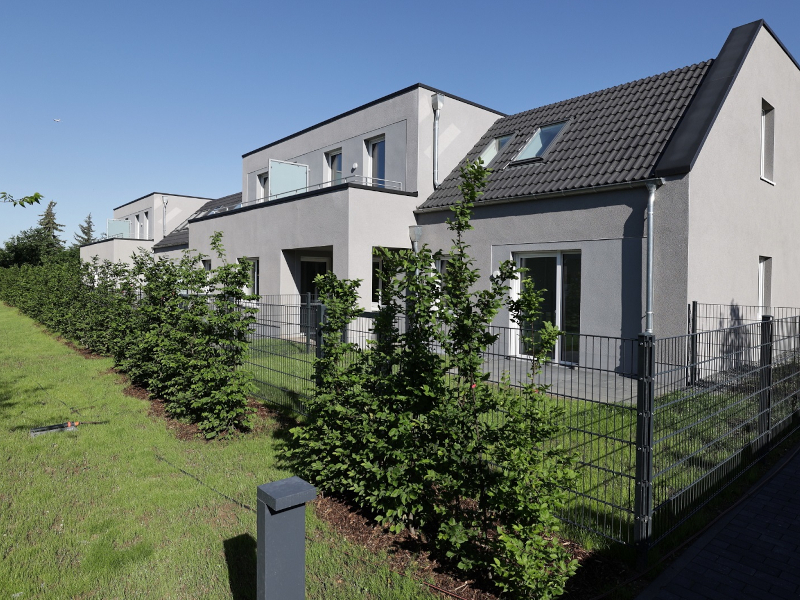 Reihe moderner Doppelhäuser in einem Vorstadtumfeld, mit privaten Gärten und Zäunen, die zeitgemäßes Wohnen mit Gemeinschaftsgefühl verbinden.