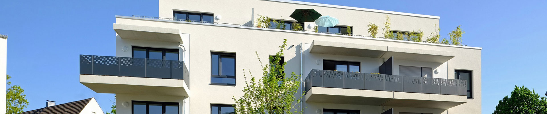 Modernes Mehrfamilienhaus in der Eythstraße mit mehrstöckiger Architektur, Balkonen und einer Dachterrasse, die mit grünen Pflanzen ausgestattet ist.